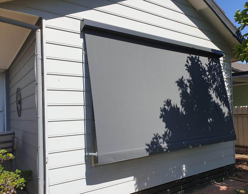 Straight-drop sun blind in side guides shading a weatherboard home window
